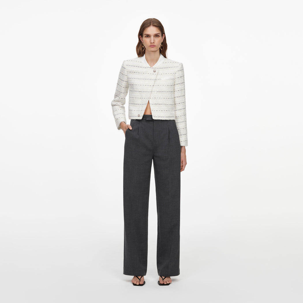 Woman wearing a white tweed cropped jacket with an asymmetrical closure and dark grey wide-leg trousers