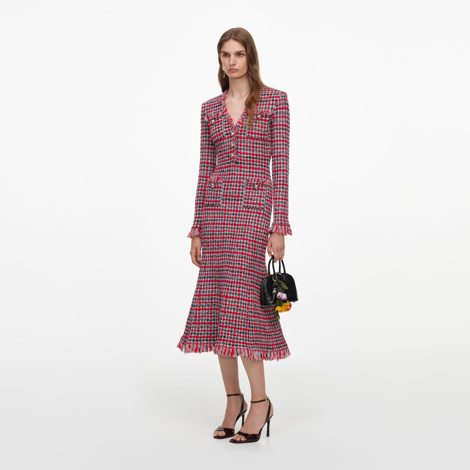 Woman in a red, black, and white tweed dress with gold buttons and fringe trim, holding a black handbag