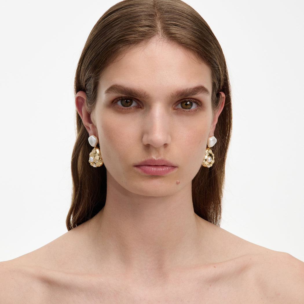 Woman with long brown hair wearing gold earrings with white pearls and small clear stones