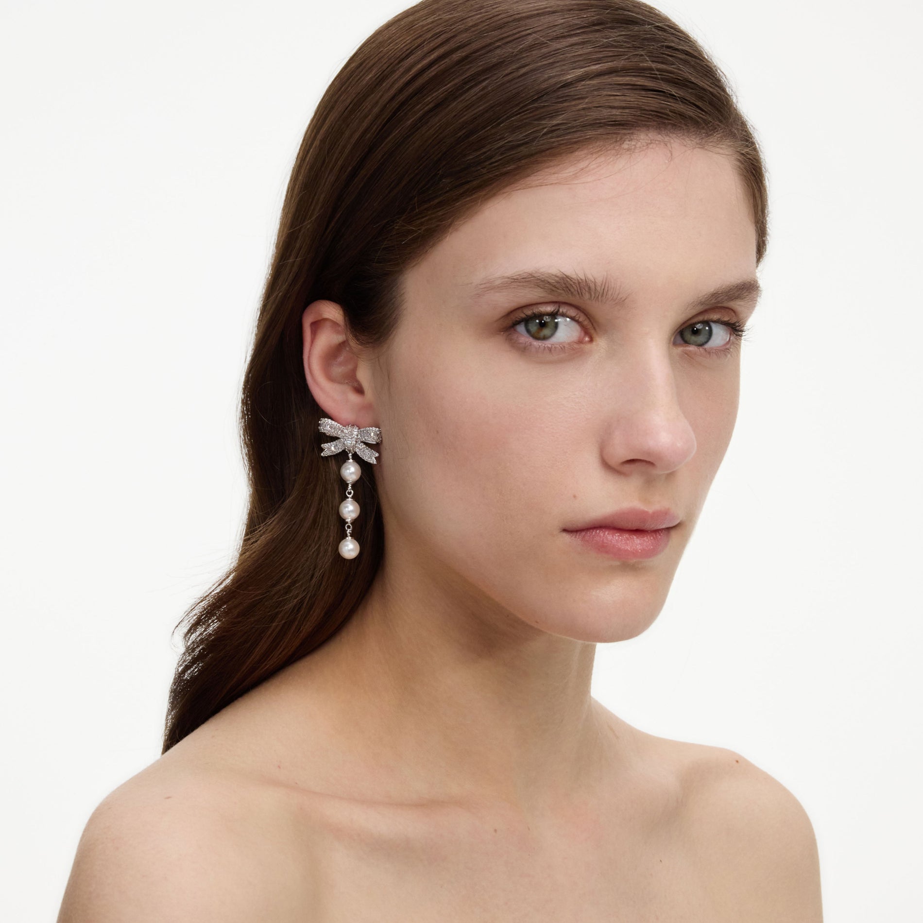 A close up of a woman wearing the Crystal Bow Pearl Droplet Earrings
