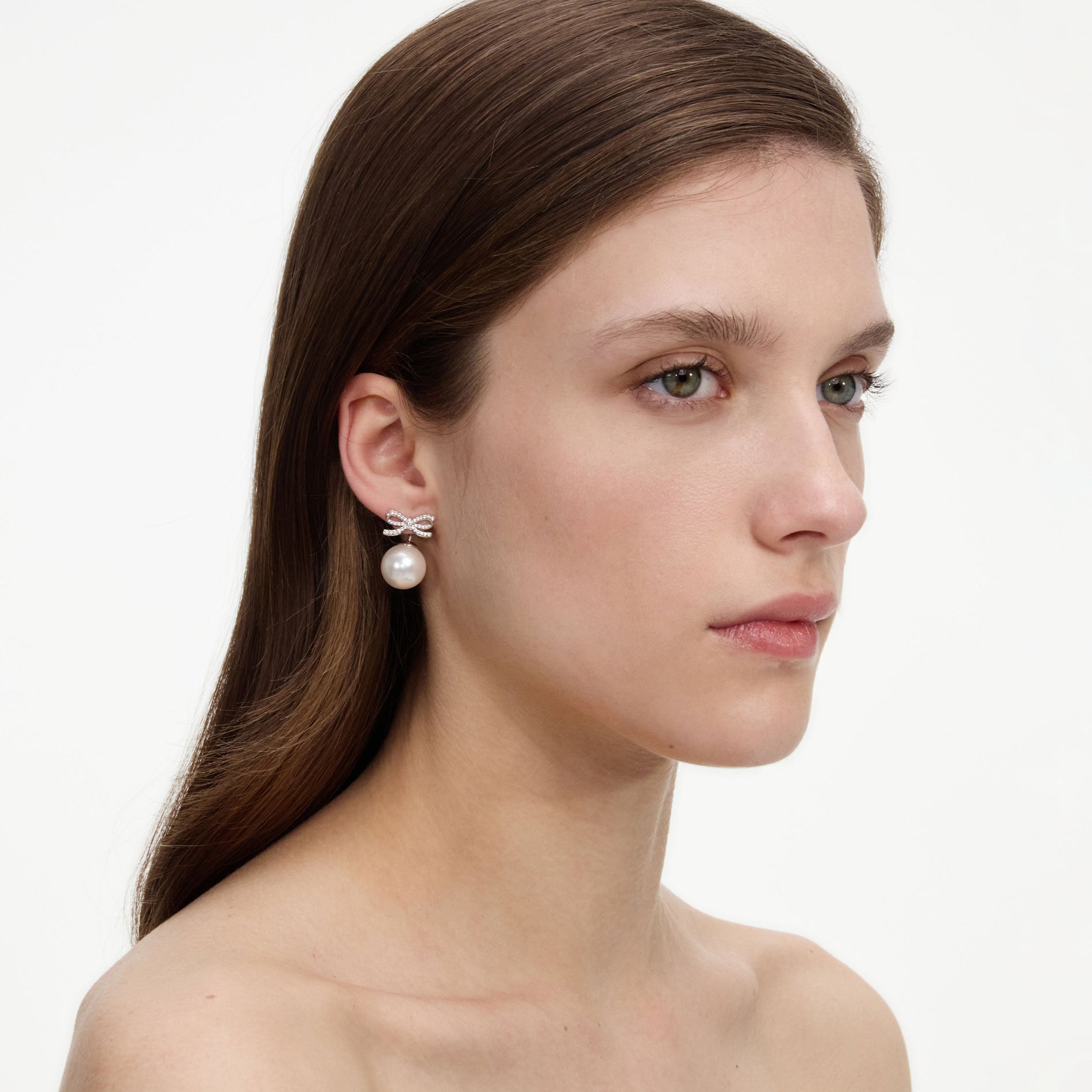 A close up of a woman wearing the Crystal Bow Pearl Back Earrings
