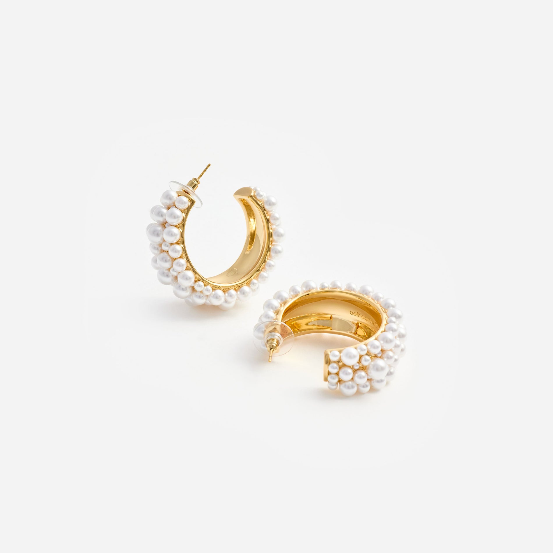 Two gold hoop earrings with white pearls on a white background
