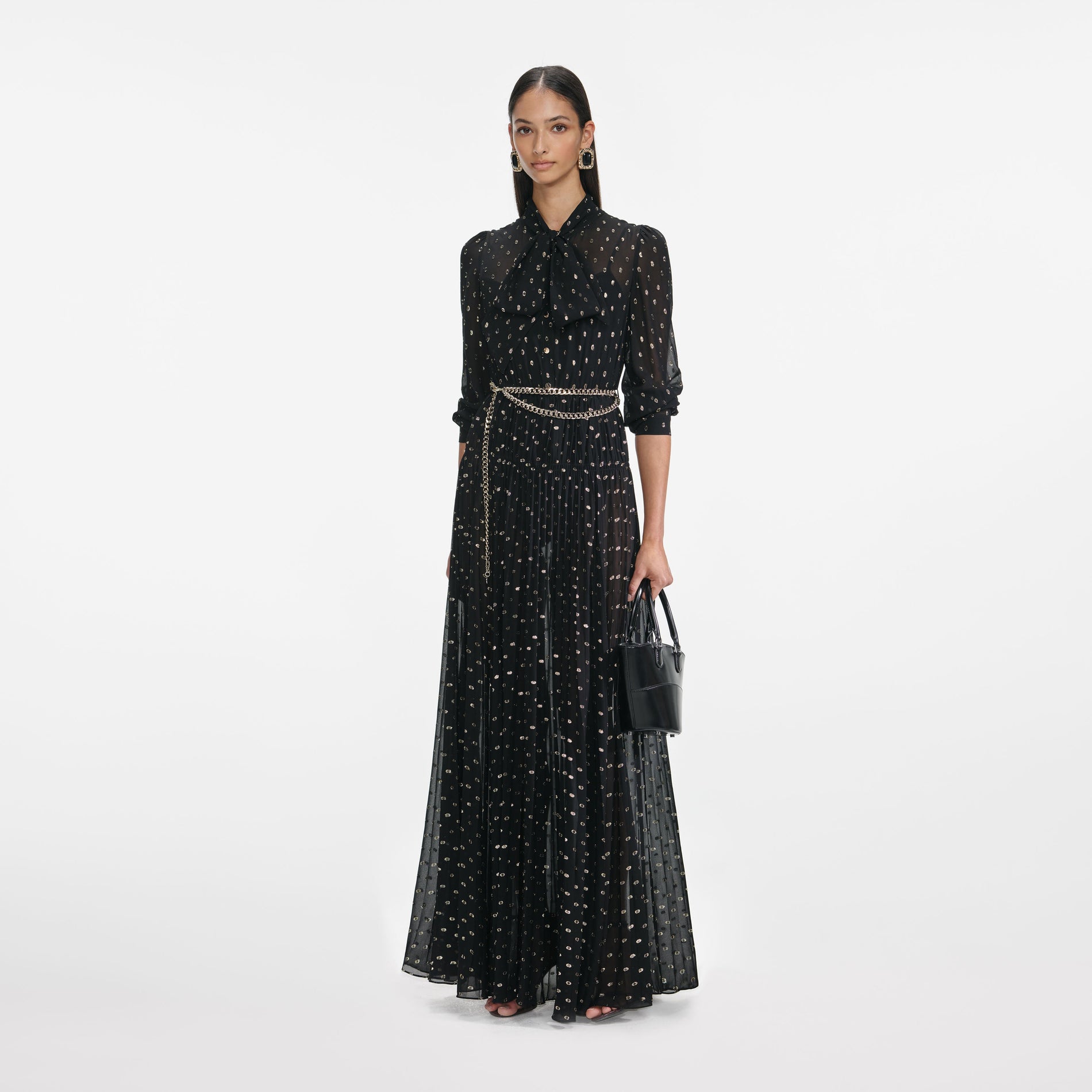 Side view of a woman wearing the Black And Gold Pussy Bow Maxi Dress