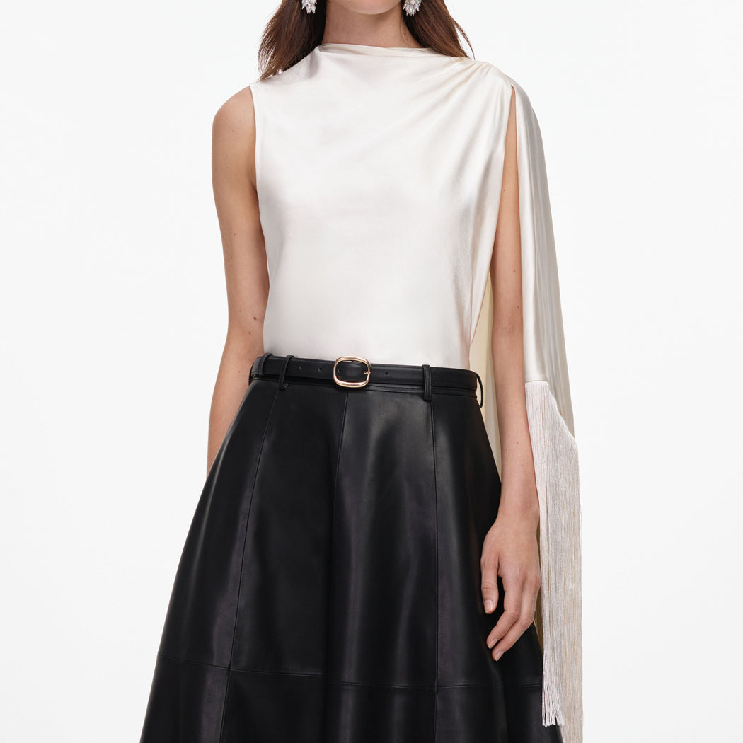Woman in white sleeveless top with draped neckline and fringe detail, black leather skirt with belt