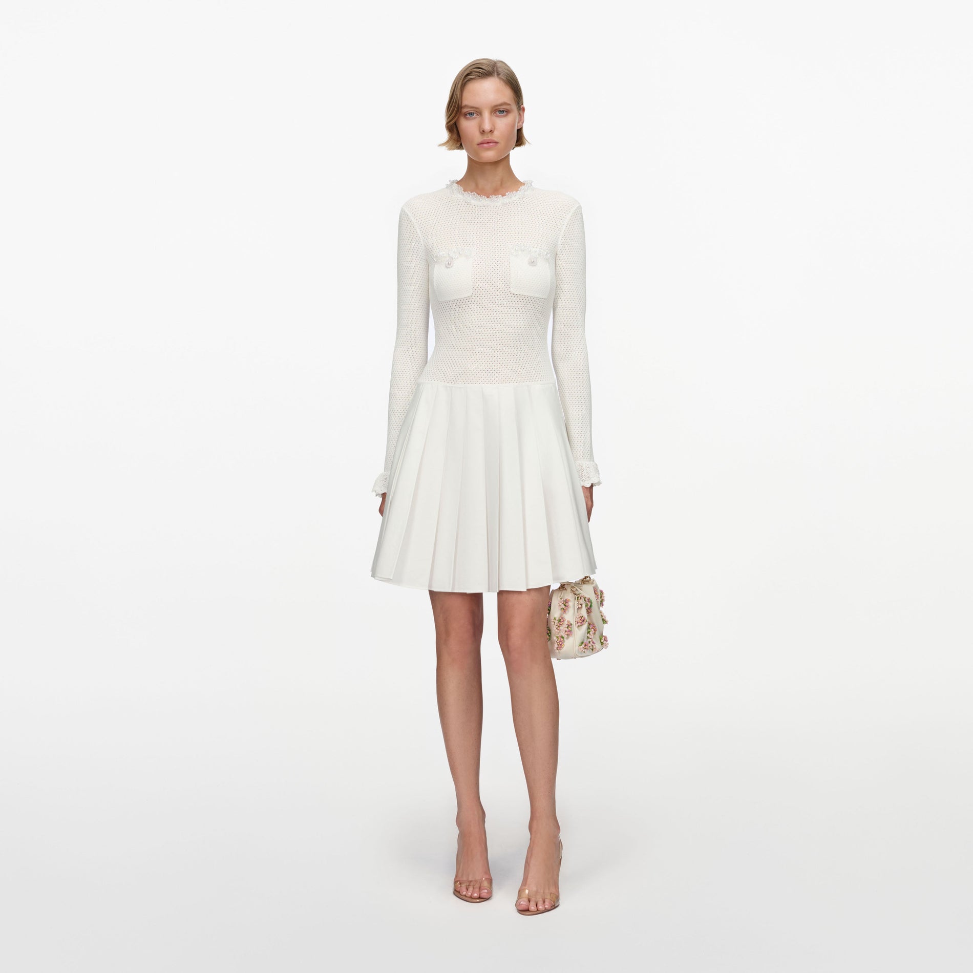 Woman in white long-sleeved mini dress with pleated skirt and floral handbag