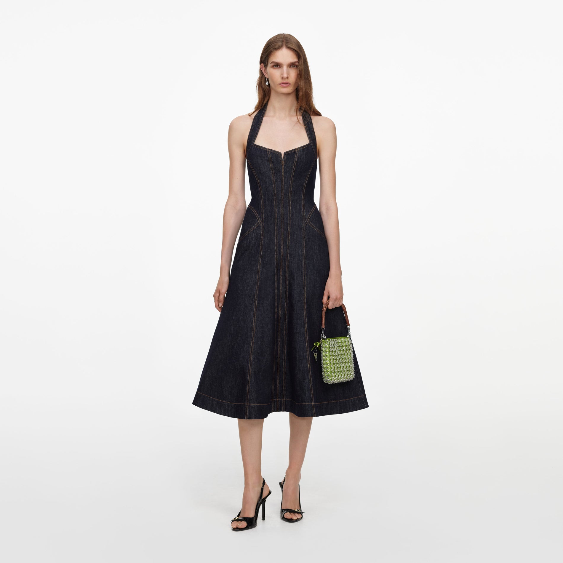 Woman in a dark denim halter dress with a green beaded handbag and black slingback heels