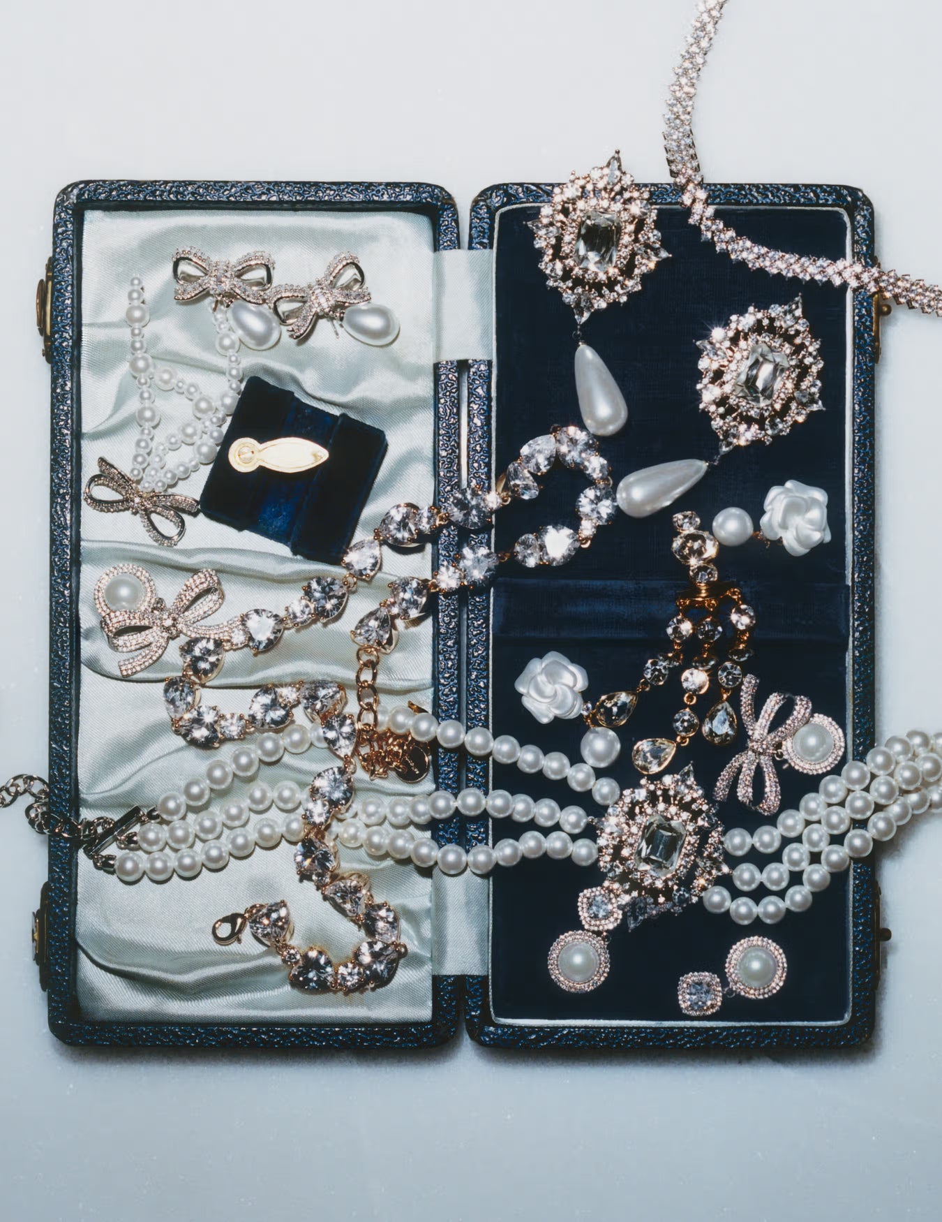 Open jewellery box with various pearls and jewellery on a grey background.