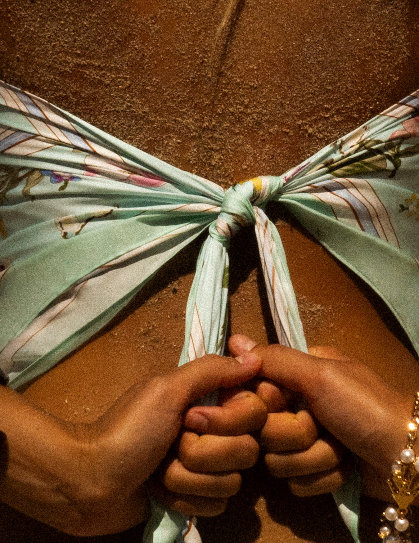 Close-up of hands tying a floral mint scarf.