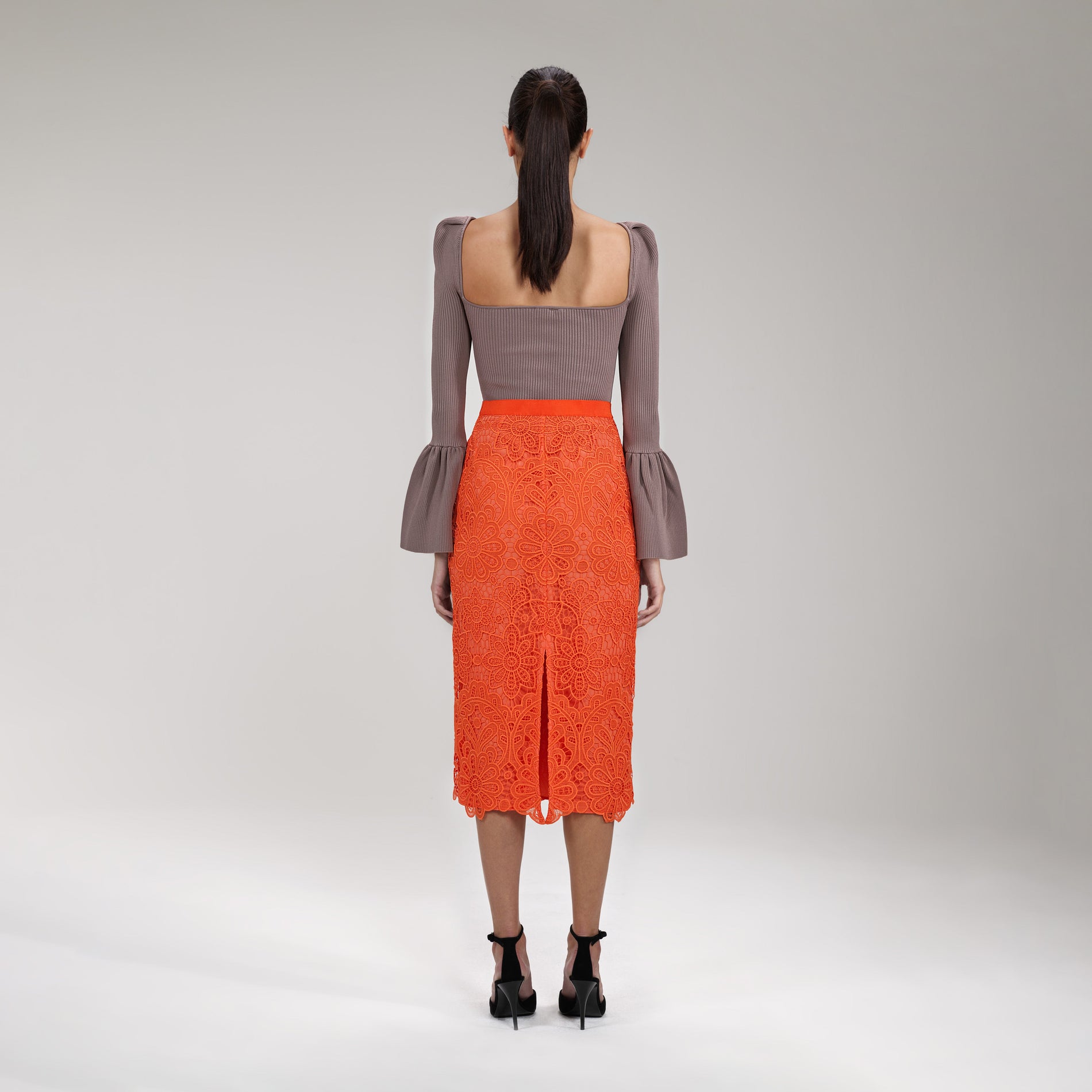 A woman wearing the Orange Floral Guipure Midi Skirt