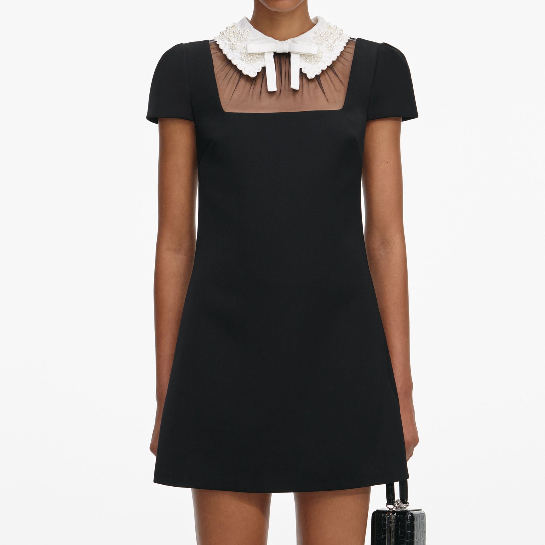 A close up of a woman wearing the Black Crepe Bow Collar Mini Dress